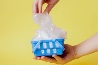 sarı arka plan üzerinde alışveriş sepeti elinde polietilen çanta