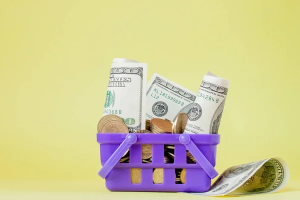 Winkelmandje met munten en dollar rekeningen op gele achtergrond — Stockfoto