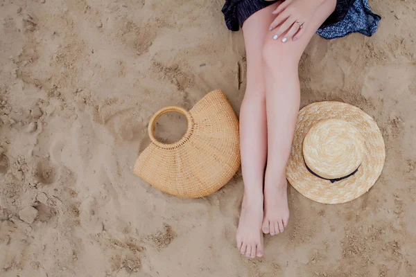 Piernas bronceadas de mujer, sombrero de paja y bolso en playa de arena. Concepto de viaje. Relajarse en una playa, con los pies en la arena . — Foto de Stock