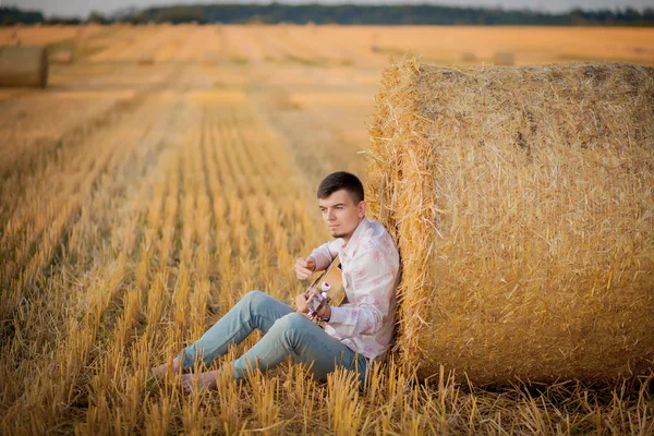 Młody facet jest relaksujący na wsi z gitarą. Gra th — Zdjęcie stockowe