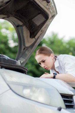 Arabası bozulduktan sonra yol kenarındaki genç kadın hasarı görmek için kaputu açtı.