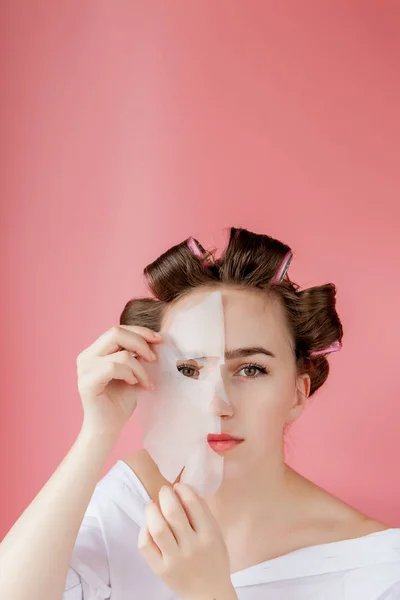 Menina bonita com uma máscara e curlers tocando seu rosto . — Fotografia de Stock