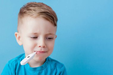 Termometresi olan hasta bir çocuk ateşinin yüksekliğini ölçüyor ve kameraya bakıyor.