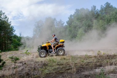 Sarı dörtlü Atv'ye binen adam kumlu bir ormanda tüm arazi aracına biniyor. Ekstrem spor hareketi, macera, turistik.