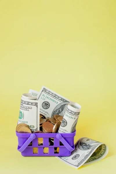 Winkelmandje met munten en dollar rekeningen op gele achtergrond. Ruimte voor tekst. Close-up. Business concept. — Stockfoto