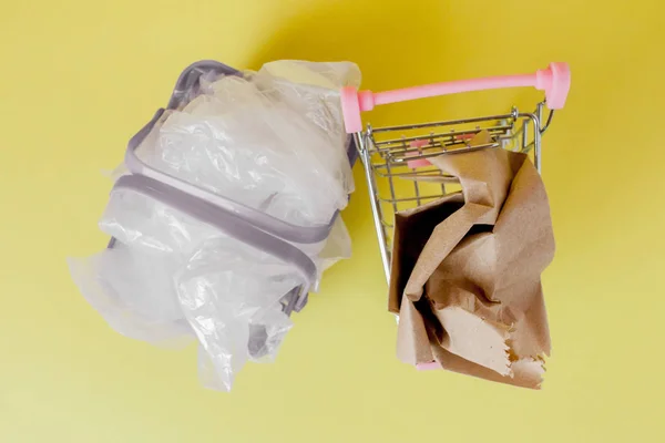 Polyethylenu ve výši a papírové tašky v nákupním košíku na žlutém pozadí — Stock fotografie