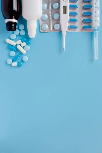 Treatment of colds and flu. Various medicines, a thermometer, sprays from a stuffy nose and a pain in a throat on a blue background. Copy space. Medicine flat lay