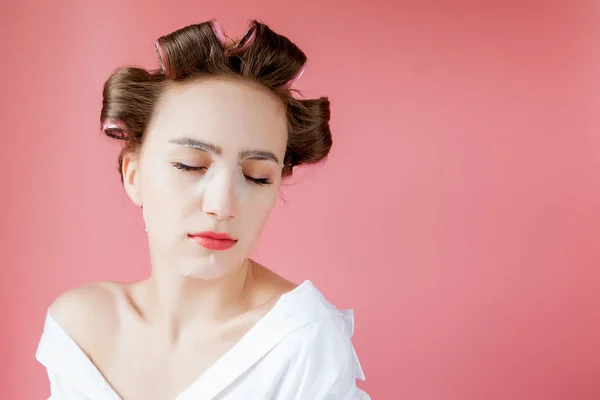 Menina bonita com uma máscara e curlers tocando seu rosto . — Fotografia de Stock