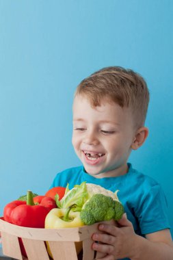 Mavi arka planda taze sebze ile çocuk tutan sepet. Sebze