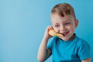 Little Boy tries to speak by means of a banana instead of phone. clipart