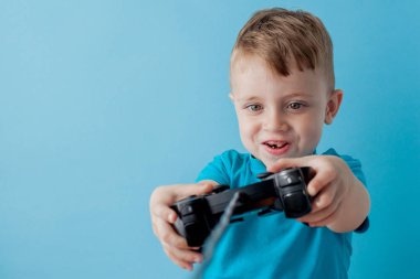 Küçük çocuk çocuk 2-3 yaşında mavi giysiler giyen gameson mavi arka plan çocuk stüdyo portre için el joystick tutun. İnsanlar çocukluk yaşam tarzı kavramı. Kopya alanı yla alay edin
