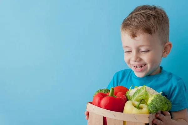 Хлопчик тримає кошик зі свіжими овочами на синьому фоні. Вегас — стокове фото