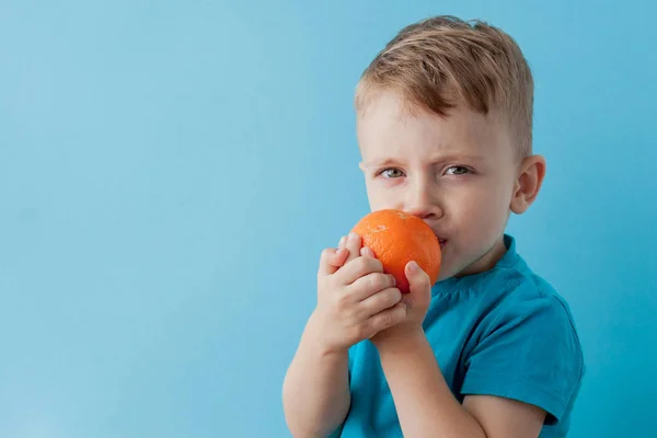 Niño pequeño sosteniendo una naranja en sus manos sobre fondo azul, di — Foto de Stock