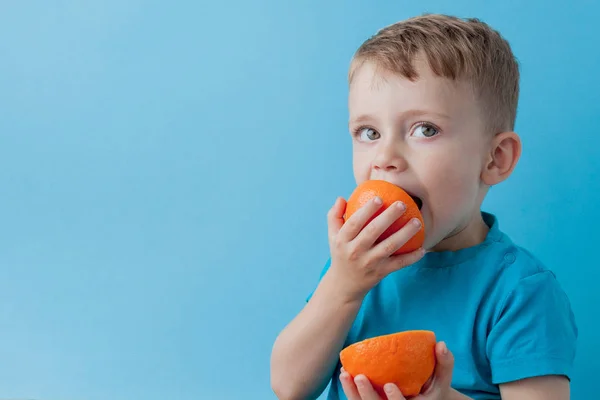 Niño pequeño sosteniendo una naranja en sus manos sobre fondo azul, di — Foto de Stock