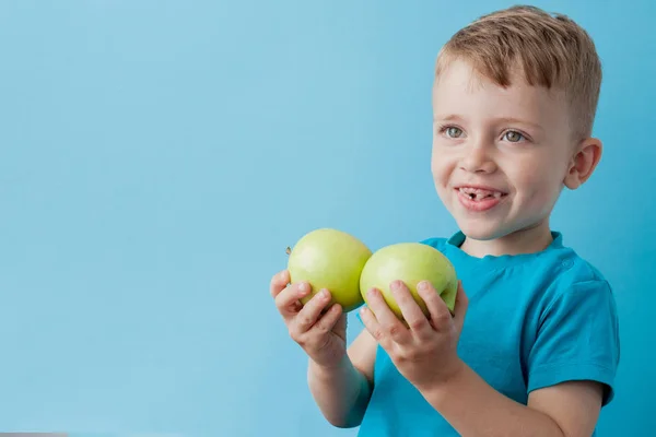 Menino segurando uma maçã em suas mãos no fundo azul, di — Fotografia de Stock