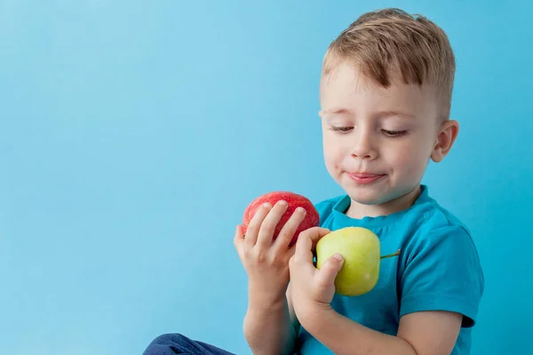 Niño pequeño sosteniendo una manzana en sus manos sobre fondo azul, di — Foto de Stock