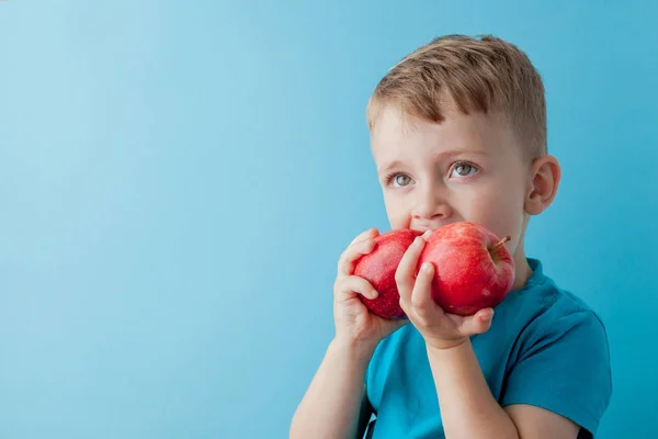 Маленький хлопчик тримає яблука в руках на синьому фоні, бл — стокове фото