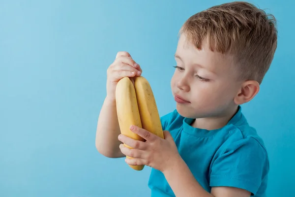 Маленький хлопчик тримає і їдять банан на синьому фоні, продовольчої, дієти і здорового харчування концепцію — стокове фото
