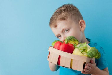 Mavi arka planda taze sebze ile çocuk tutan sepet. Sebze