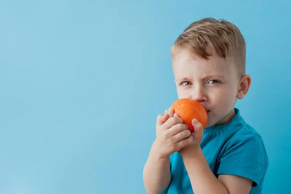 Niño pequeño sosteniendo una naranja en sus manos sobre fondo azul, di — Foto de Stock
