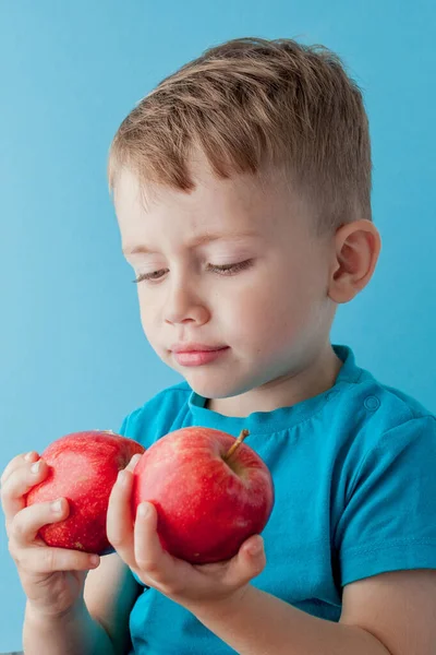 Liten pojke som håller en äpplen i händerna på blå bakgrund, di — Stockfoto