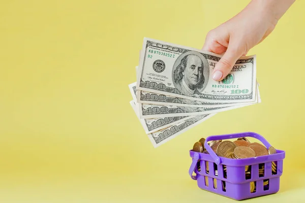 Warenkorb mit Münzen und Dollarscheinen in der Hand auf gelbem b — Stockfoto