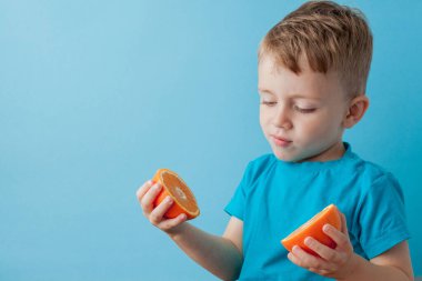 Mavi arka planda elinde portakal tutan küçük çocuk, iyi sağlık kavramı için diyet ve egzersiz yapıyor.