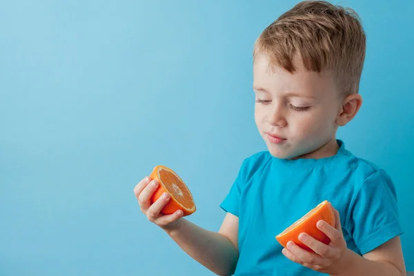 Niño sosteniendo una naranja en sus manos sobre fondo azul, dieta y ejercicio para un buen concepto de salud — Foto de Stock