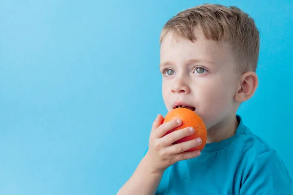 Маленький хлопчик тримає помаранчевий в руках на синьому фоні, дієту і фізичні вправи для хорошої концепції здоров'я — стокове фото
