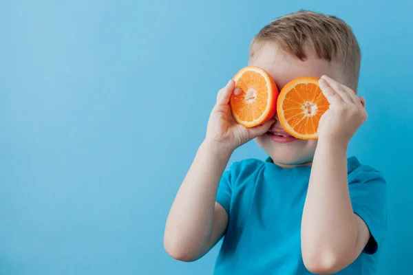 Kisfiú kezében egy narancs kék háttér, diéta és a testmozgás a jó egészség koncepció — Stock Fotó