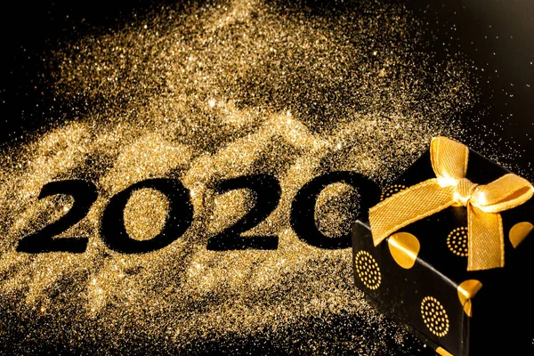 Happy New Year 2020 . Creative Collage of numbers two and zero made up the year 2020. Beautiful sparkling Golden number 2020 and gift on black background for design