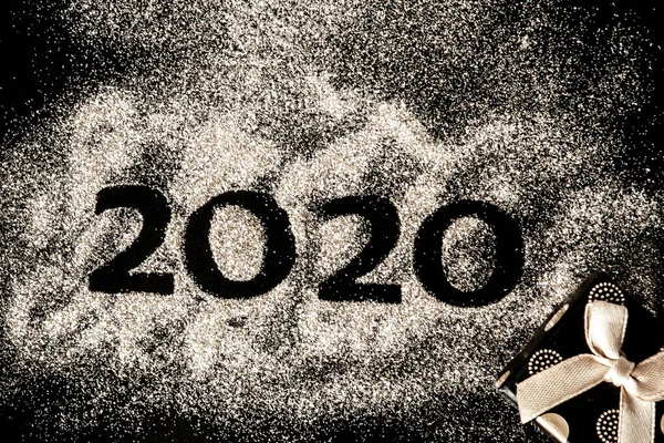 Happy New Year 2020 . Creative Collage of numbers two and zero made up the year 2020. Beautiful sparkling Golden number 2020 and gift on black background for design