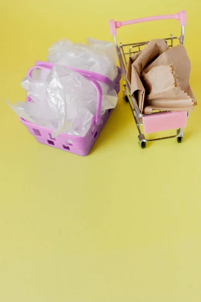 Polytheen en papieren zakken in een winkelmandje op een gele achtergrond — Stockfoto