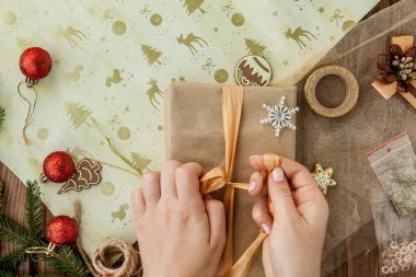 Noel hediyesini paketleyen kadınların elleri, kapatın. Ahşap arka planda hazırlıksız noel hediyeleri dekor unsurları ve eşyalarla, üst manzara. Noel ya da Yeni Yıl Kutlama Konsepti.