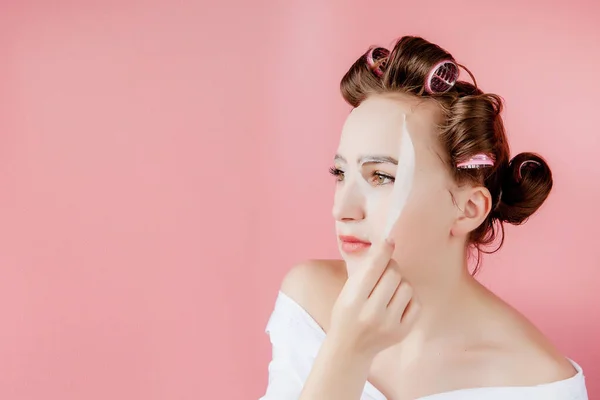 Menina bonita com uma máscara e curlers tocando seu rosto . — Fotografia de Stock