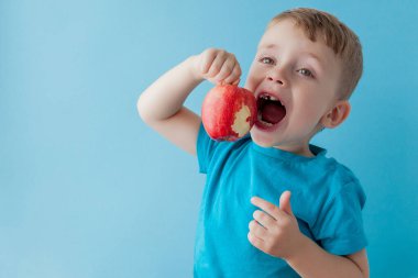 Bebek kucağında, mavi arka planda kırmızı elma yiyor.