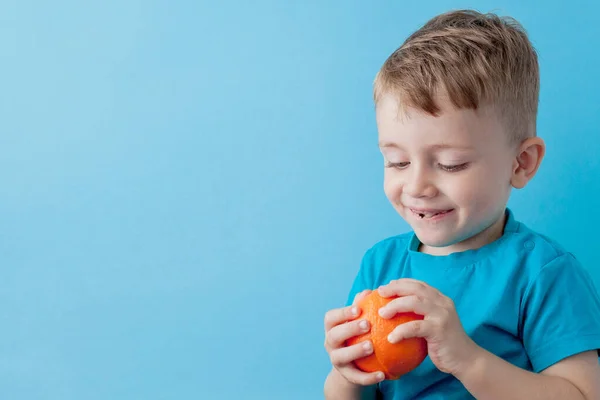 Маленький хлопчик тримає помаранчевий в руках на синьому тлі, ді — стокове фото