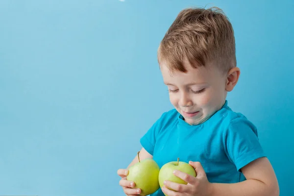 Menino segurando uma maçã em suas mãos no fundo azul, di — Fotografia de Stock
