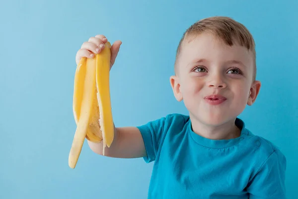 Little Boy Segurando e comendo uma banana no fundo azul, comida — Fotografia de Stock