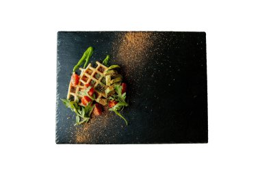 Taze pişmiş Belçika waffle 'ı roka, domates ve siyah üzerine avokado beyaz arka planda izole edilmiş bir tabak. Lezzetli waffle. Kahvaltı konsepti. Sağlıklı kahvaltı..