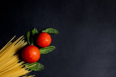 Spagetti macunu, domates ve diğer ürünler koyu arka planda yemek pişirmek için. Metin için boşluk, üst görünüm.