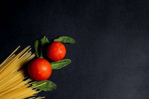 Spaghetti paste, tomato and other products for cooking on dark background top view. Space for text, top view.