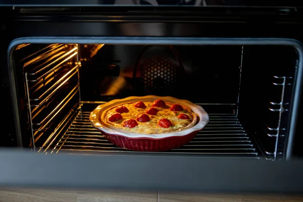pie with chicken and tomatoes is on a baking sheet in the oven. quiche loren.