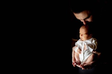 Babası 15 günlük oğlunu siyah arka planda elinde tutuyordu. Bebek babasının üzerine yatıyor. Tatil kavramı baba, boşluğu kopyala.