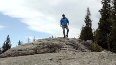 Genç, kaygısız çocuk kayalara tırmanıyor, tepeye ulaşmayı kolaylaştırmak için sırıkları kullanıyor, yoldaki doğal harikaların tadını çıkarıyor..