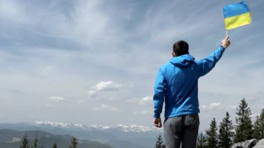 Adam elinde bir Ukrayna bayrağı, ağır çekimde Carpathian dağlarının parlak tepesinde sallanıyor.