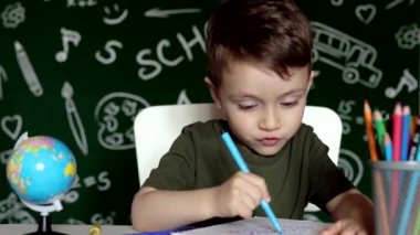 Anaokulu çocuğu okul ödevi yapıyor. Okul malzemeleriyle masasının yanında gülen surat ifadesi olan okul çocuğu. Eğitim. Önce eğitim. Okul kavramı.