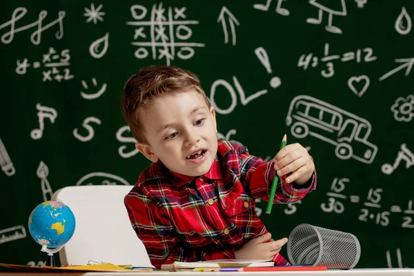 学龄前男孩在学校做作业。一个满脸喜色的学童在课桌旁拿着学习用品.教育。教育第一。学校概念. — 图库照片