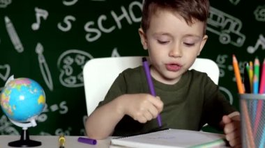 Anaokulu çocuğu okul ödevi yapıyor. Okul malzemeleriyle masasının yanında gülen surat ifadesi olan okul çocuğu. Eğitim. Önce eğitim. Okul kavramı.