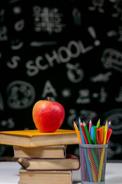 Kitaplar, kalemler ve beyaz masanın üzerindeki elmayla okula geri dön.
